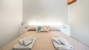 A bed with a quilted cover, two pillows, and folded towels. - Mia Rooms: Double Room with Private Patio (Villasimius)