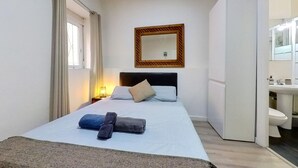 Una camera d'albergo con un letto, un comodino, uno specchio e un bagno parzialmente visibile attraverso una porta aperta.