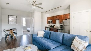 Uma sala de estar moderna com um sofá azul, uma mesa de centro e um espaço de refeições com cadeiras.