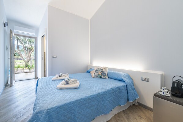 Un dormitorio con cama, mesita de noche, ventana y puerta.