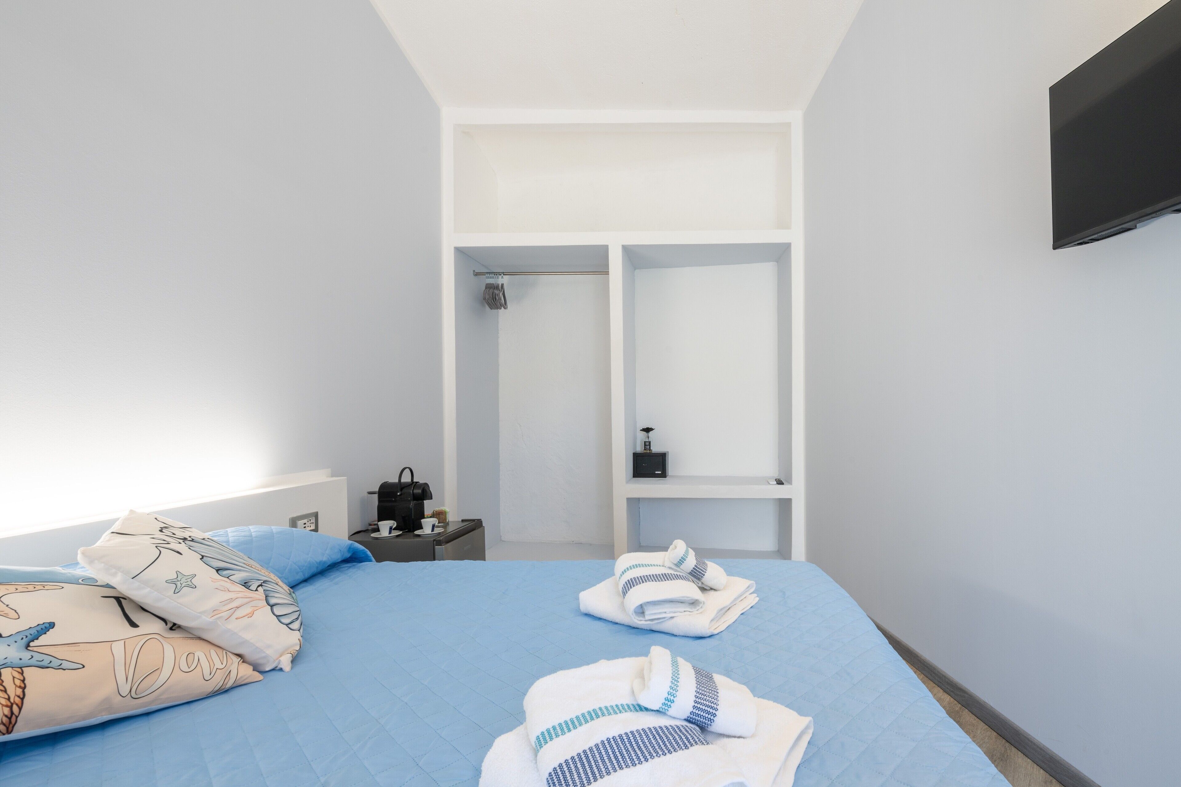 A hotel room with a bed, a nightstand, a TV, a wardrobe, and a shower area.