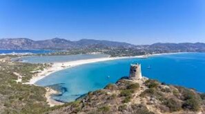 Un paisaje costero con una torre destacada en una colina, una playa arenosa y un mar azul y despejado.
