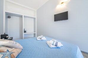 Habitación de hotel con cama, televisor de pantalla plana, armario y escritorio con lámpara.