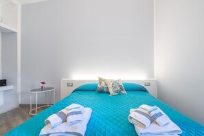 Ein Hotelzimmer mit Bett, zwei Kissen, einem kleinen runden Tisch mit Vase und einem an der Wand befestigten Regal.