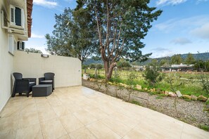 Eine Terrasse im Freien mit Sitzgelegenheit, einem Baum und Blick auf eine grüne Landschaft.