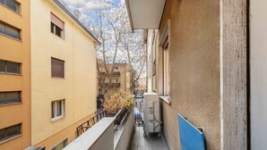 Ein schmaler Korridor mit einem Balkon, einer blauen Tür und einem Gebäude mit zahlreichen Fenstern.