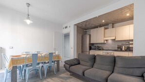 Eine moderne Küche mit Einbaugeräten, ein Essbereich mit Tisch und Stühlen sowie ein graues Sofa.