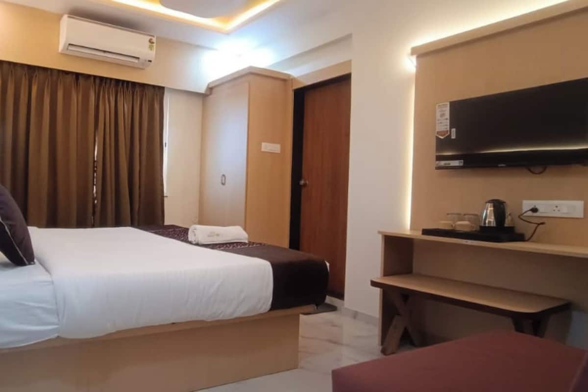 A hotel room with a bed, a TV, a desk, and a shelf with items.