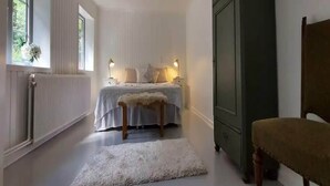 Une chambre à coucher comprenant un lit, des lampes de chevet, un radiateur, une armoire et un banc.