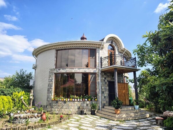 Une maison à deux étages dotée d’un balcon, d’une façade en pierre et d’un jardin agrémenté de plantes en pot.