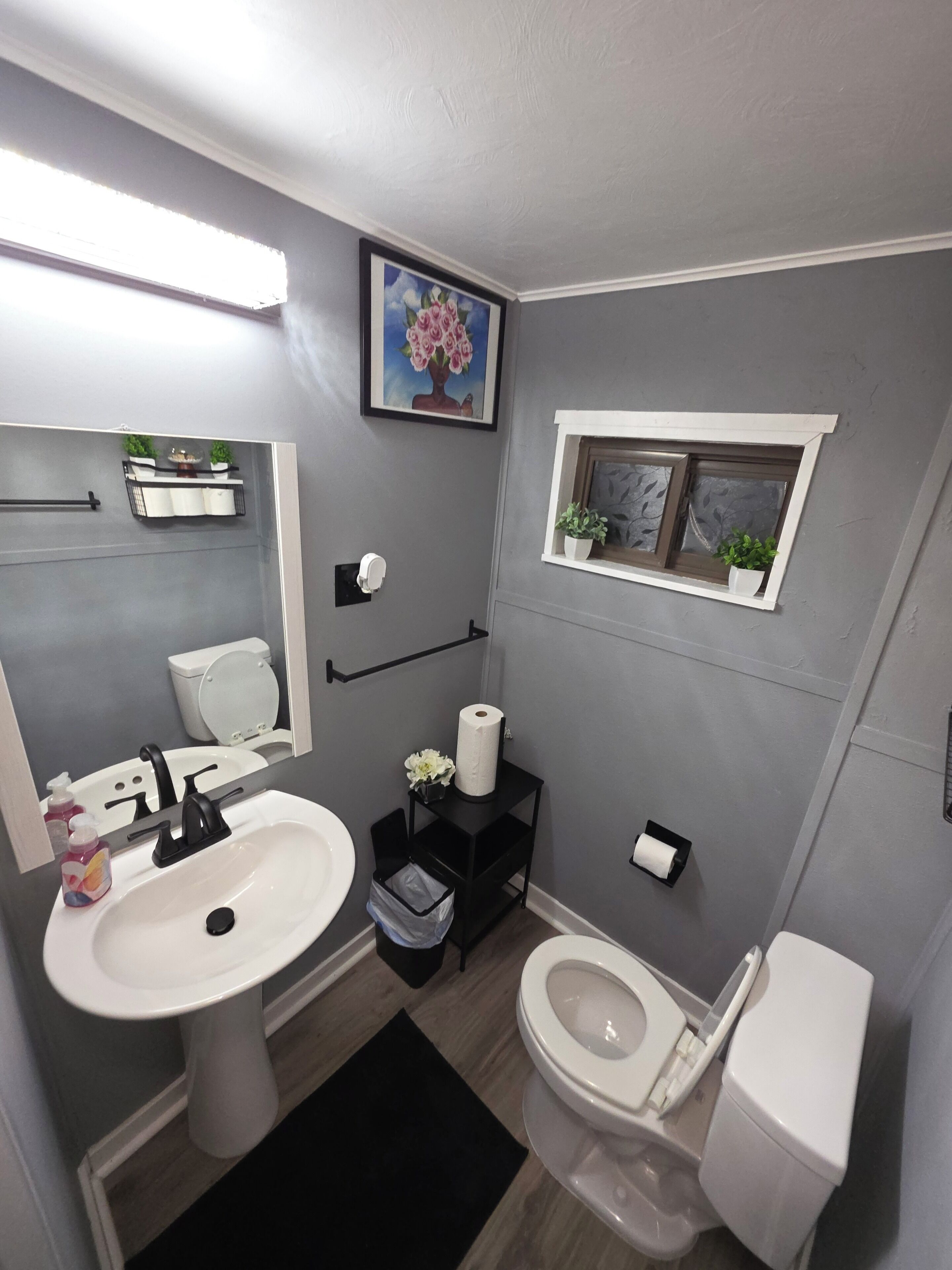 Ein modernes Badezimmer mit Waschbecken, Toilette und einem kleinen Fenster mit Pflanzen.