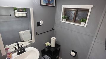 Ein modernes Badezimmer mit Waschbecken, Toilette und einem kleinen Fenster mit Pflanzen.