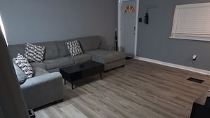 A living room with a grey sofa, patterned cushions, a coffee table, and a ceiling fan.