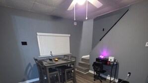 A room with a dining table, chairs, a ceiling fan, a staircase, and a desk with a computer.