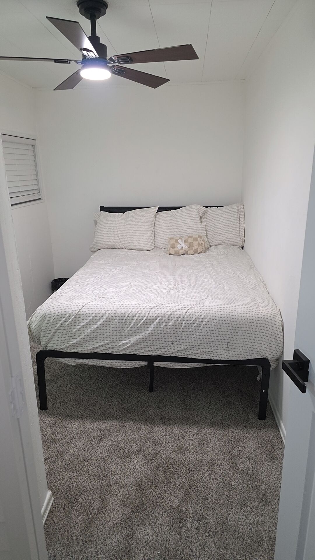 A bedroom with a bed, a ceiling fan, and a carpeted floor.