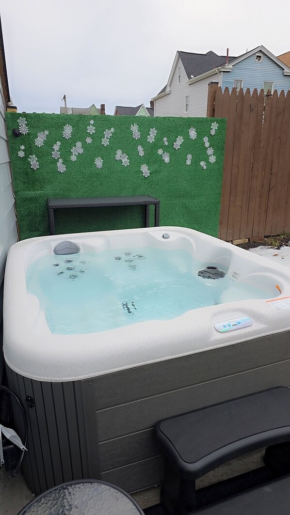 Een hottub met bedieningspaneel, voor een groene muur met sneeuwvlokdecoraties.
