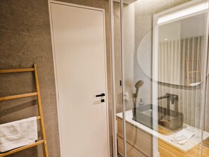 Ett badrum med en trähylla för handdukar, en vit dörr och en duschavdelning med glasväggar.