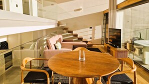 A modern living room with a round wooden table, cushioned seating, and a television. - Shell Living - Infinity Loft (FUNCHAL)