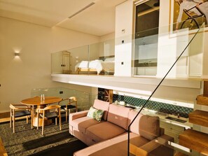 En modern lägenhet med ett sovrum i loftstil, en matplats med ett träbord och stolar samt ett litet kök med ett grönt kakel på väggen bakom arbetsbänken.