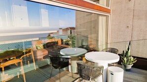 A modern outdoor seating area with a glass balustrade, a round table, and several chairs. - Shell Living - Infinity Loft (FUNCHAL)