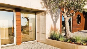 A modern building with a glass entrance, a brick column, and a tree in the foreground. - Shell Living - Infinity Loft (FUNCHAL)