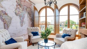 Una sala de estar acogedora con un gran mapa del mundo en la pared, asientos cómodos y vistas a través de amplias ventanas de arco.