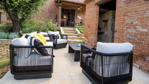 Un patio con mobiliario exterior, un edificio de ladrillo y una escalera que lleva a una puerta.