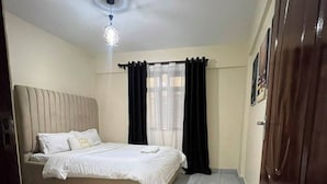 A bedroom with a bed, a window with curtains, a ceiling light, and a door.