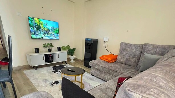 A living room with a grey sofa, a coffee table, a TV mounted on the wall, and a small white cabinet.