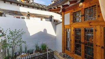 A traditional building with a wooden door and windows, a brick planter with plants, and a white wall.
