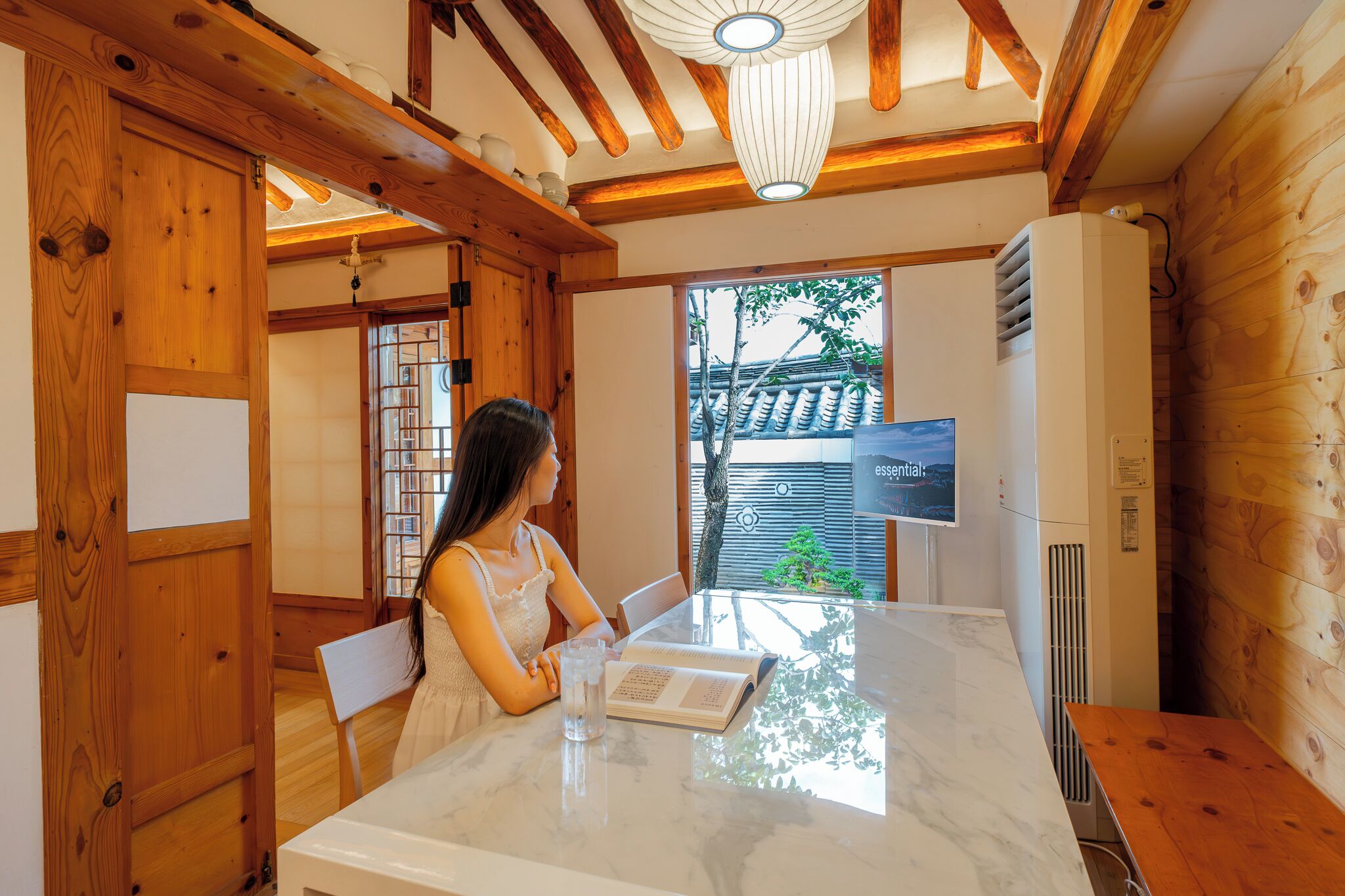 Un interior de madera con una mesa de comedor, una persona leyendo y vistas al exterior.