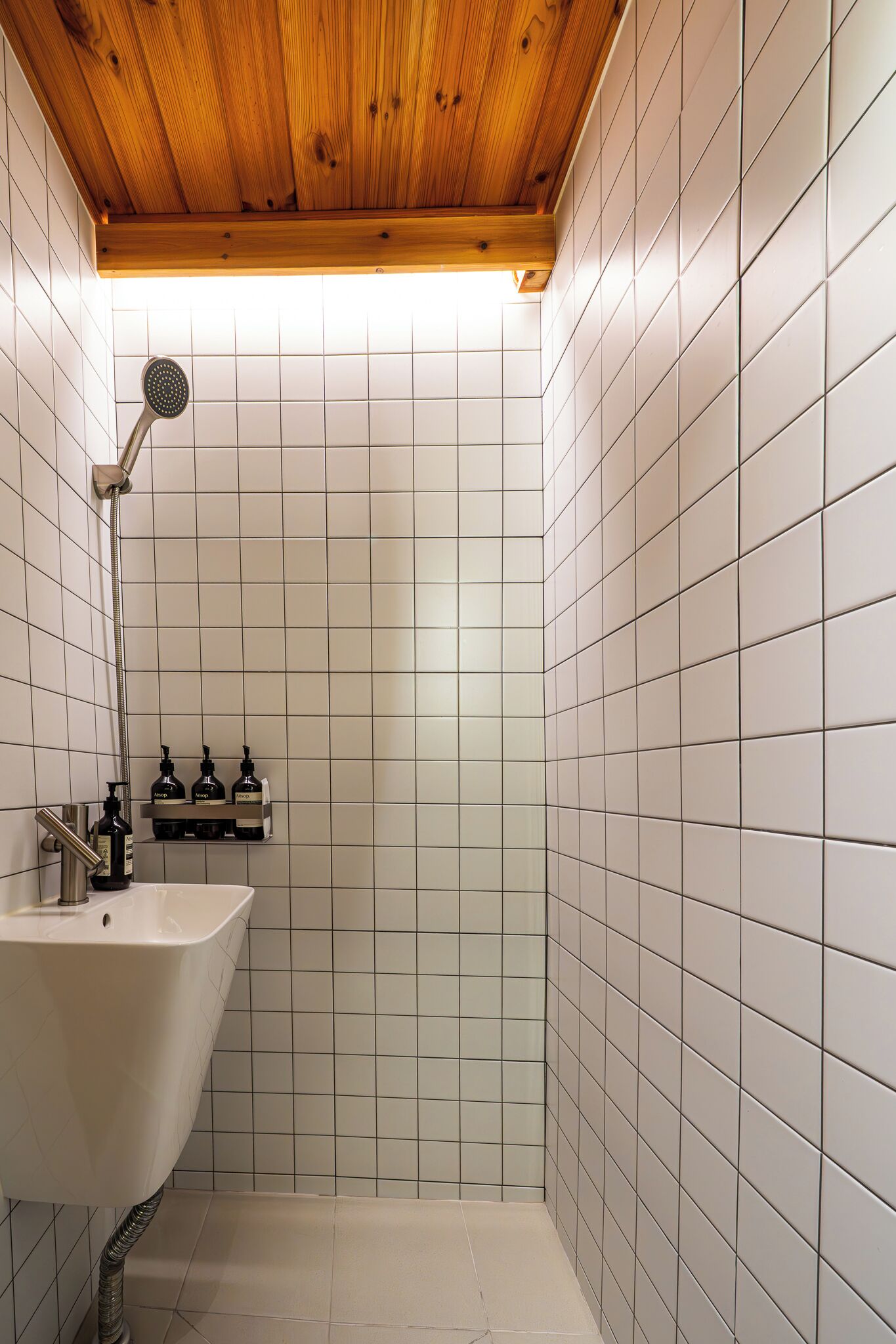 Un bagno piccolo rivestito di piastrelle, con soffitto in legno, un lavandino bianco e un soffione doccia.
