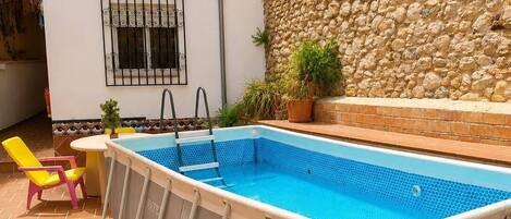 An outdoor swimming pool with a stone wall and a yellow canopy.