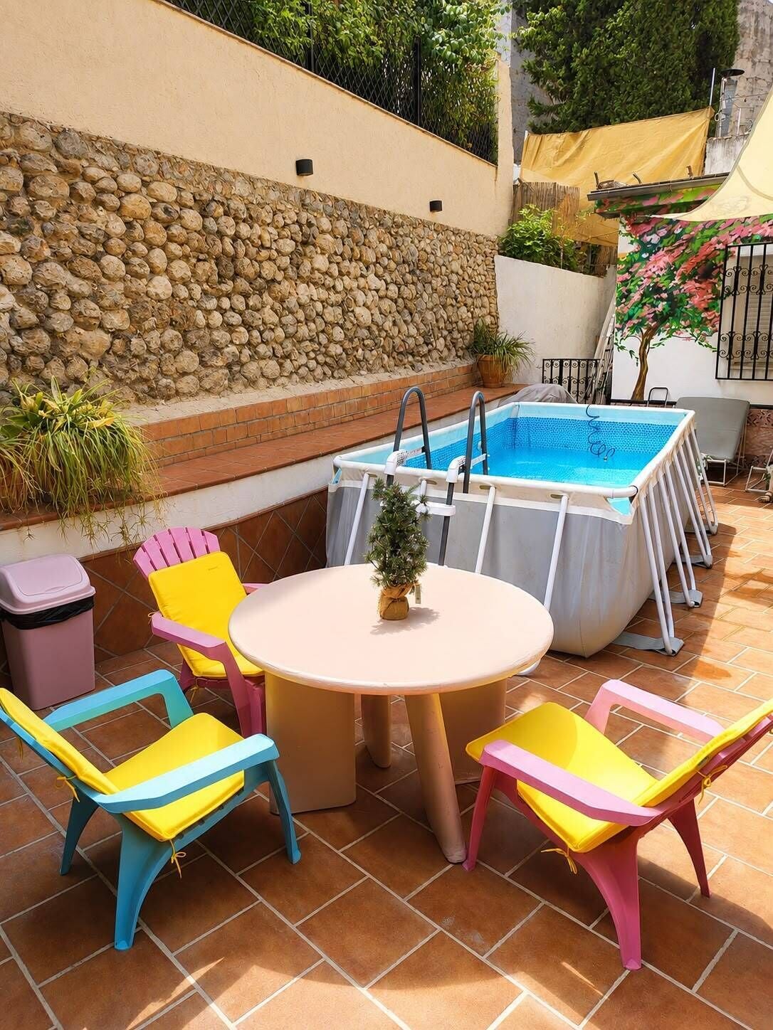 A patio with a pool, a round table, and colorful chairs.