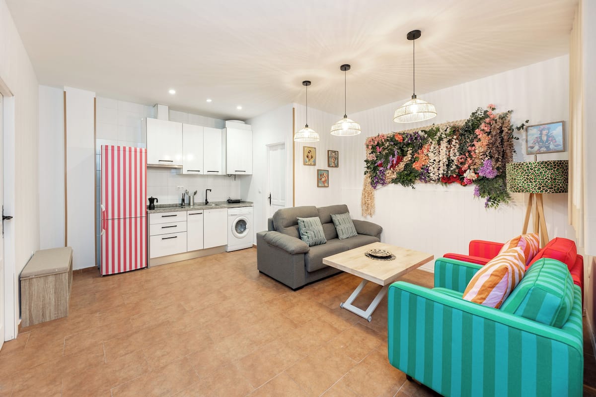 A modern kitchen with white cabinets, a striped refrigerator, and a dining area with a sofa and table.