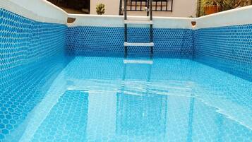 A clear blue swimming pool with a hexagonal tile pattern, a ladder leading into the pool, and a small window with decorative iron bars.