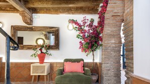 Habitació acollidora amb un butac armchair verd, un mirall amb marc de fusta i una planta en test amb flors roses.