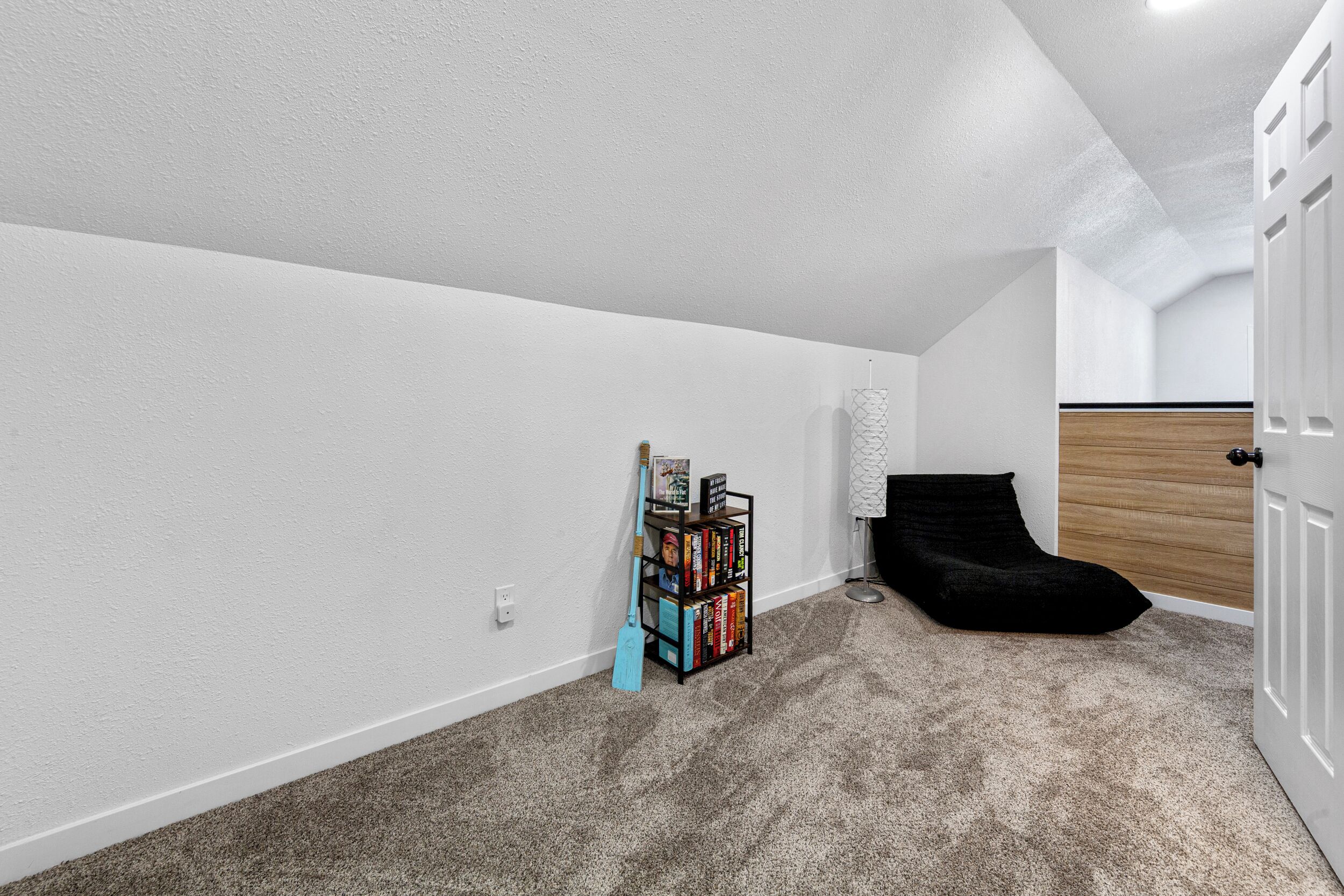 Um quarto com uma estante, uma cadeira preta e uma porta.