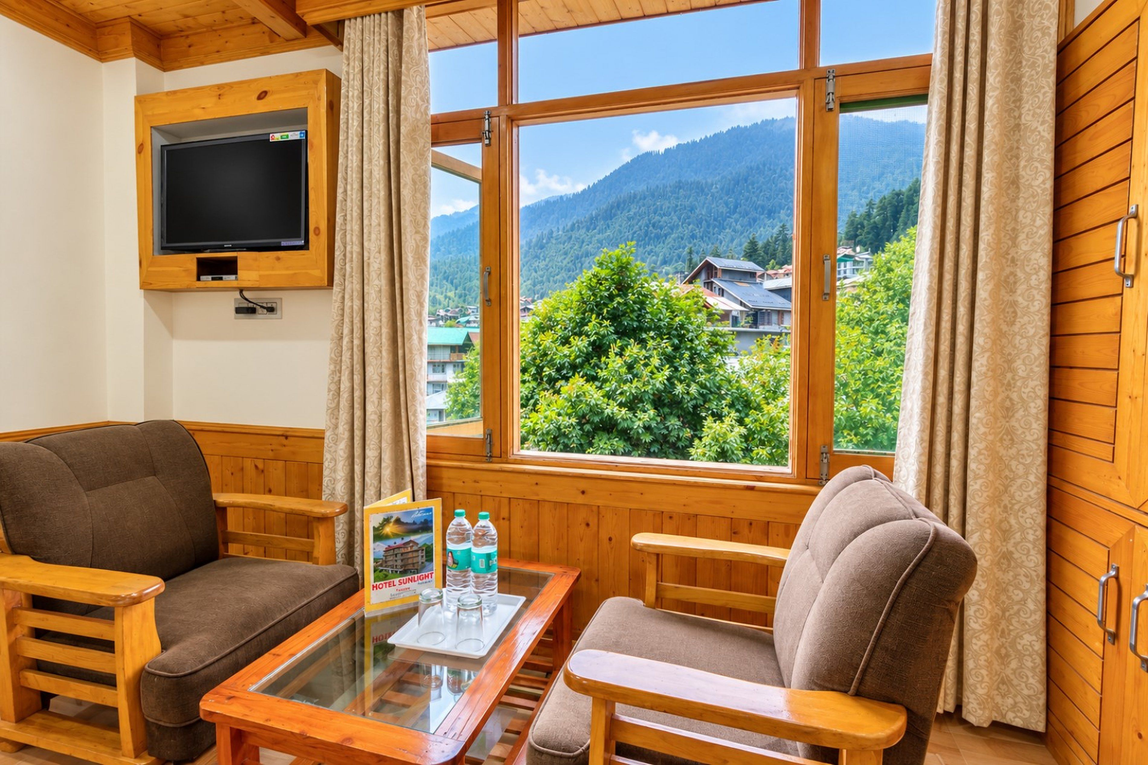 A room with wooden furniture, a television mounted on the wall, and a large window offering a view of a mountain and buildings.