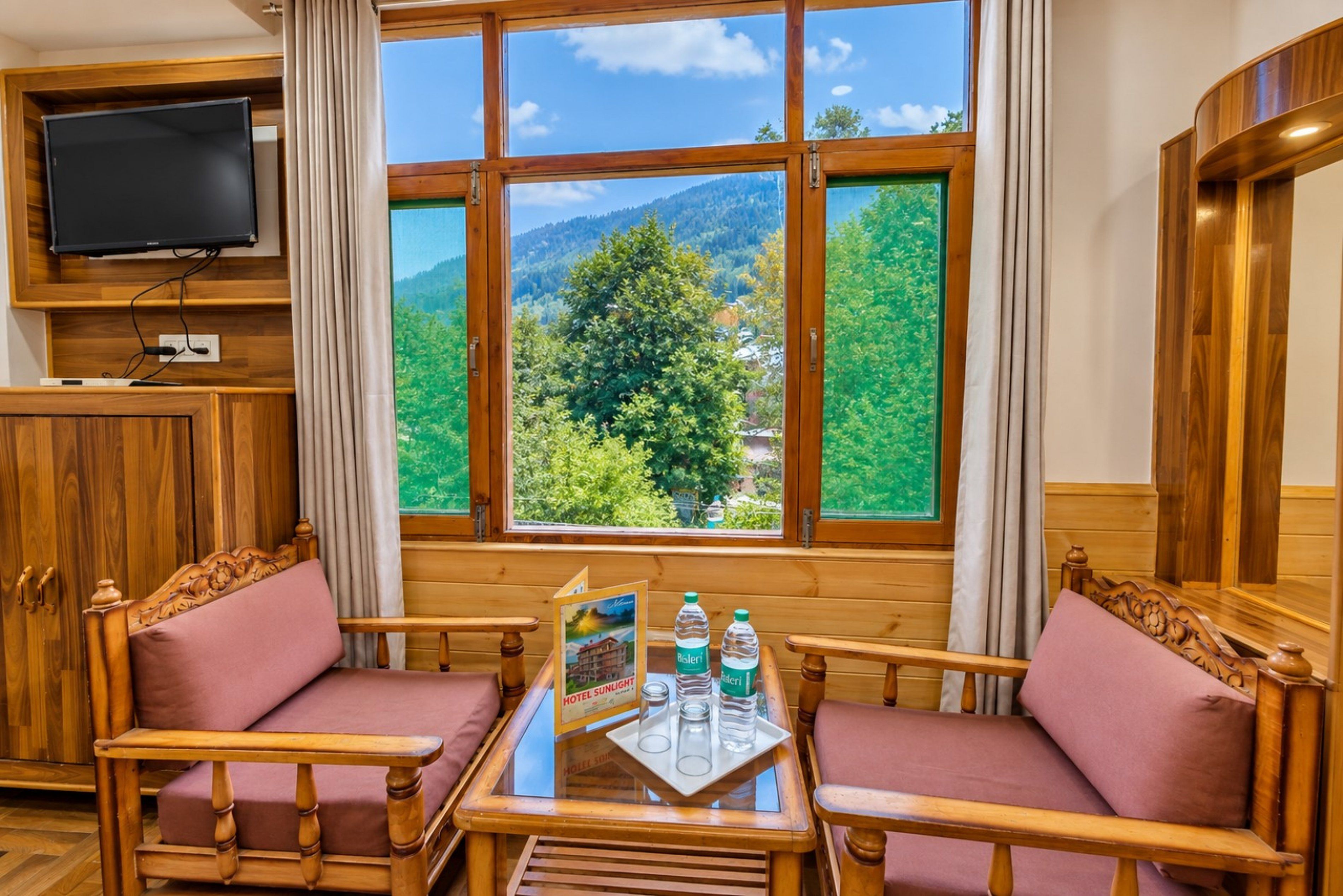 Ein Zimmer mit großem Fenster und Blick auf die Berge, einem an der Wand befestigten Fernseher sowie einem Tisch mit Glasplatte.