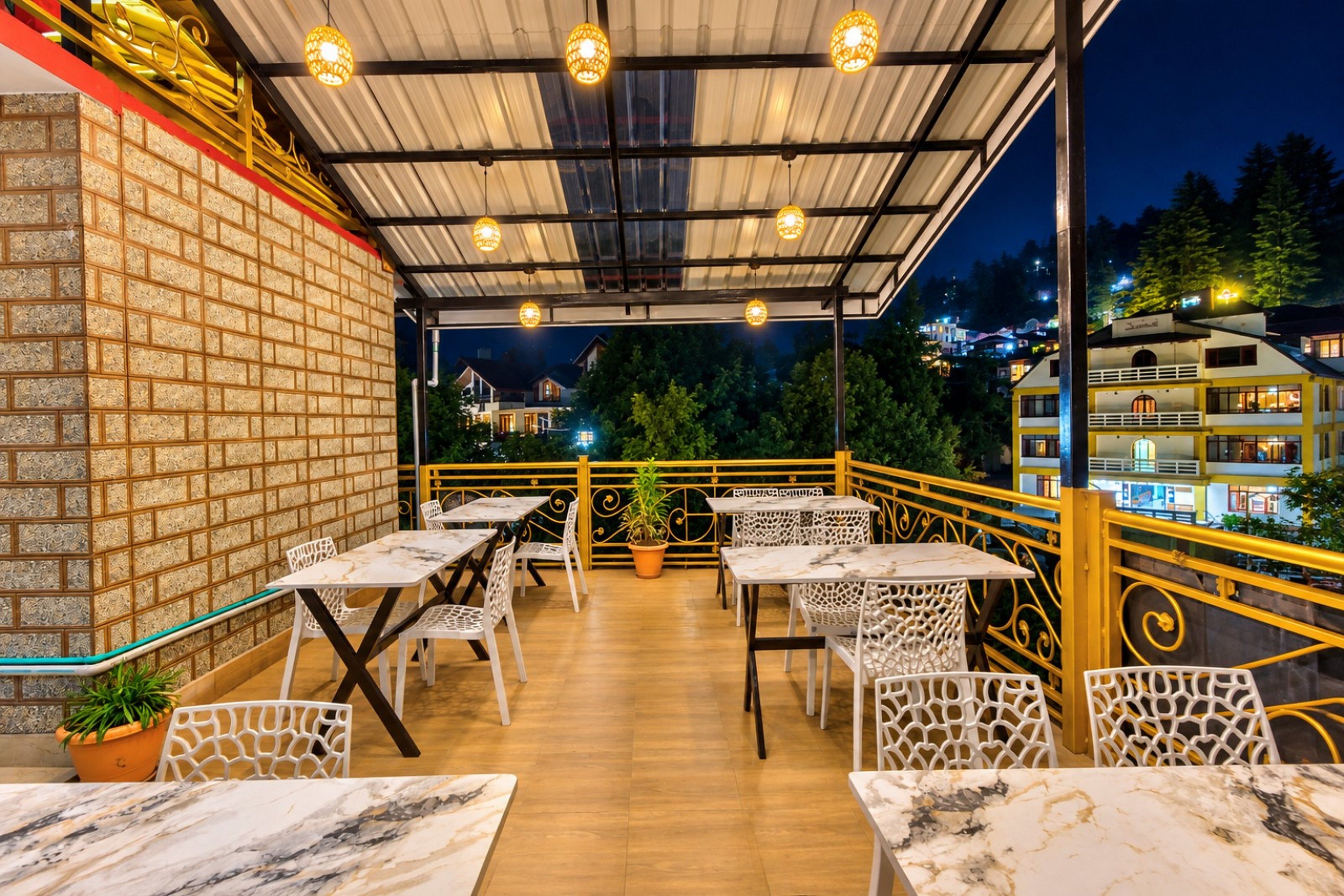 Une terrasse extérieure avec des tables et des chaises, un mur en briques et une vue sur les bâtiments en arrière-plan.