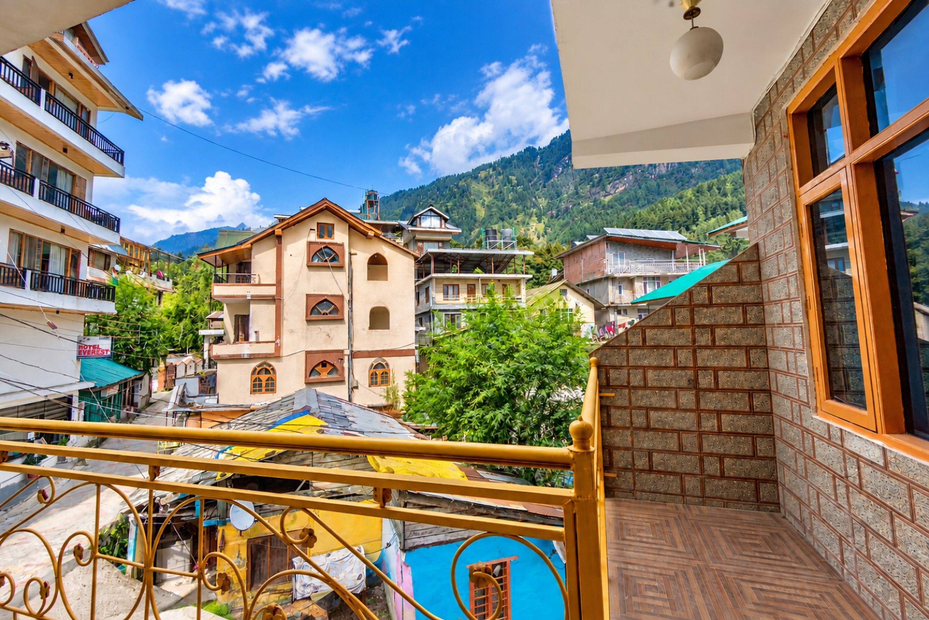 Un balcon offrant une vue sur une chaîne de montagnes, un bâtiment d’hôtel et une construction au toit bleu.