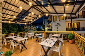 Un área de comedor al aire libre con mesas y sillas, techo cubierto y un edificio con un letrero que dice 'HOTEL E'.