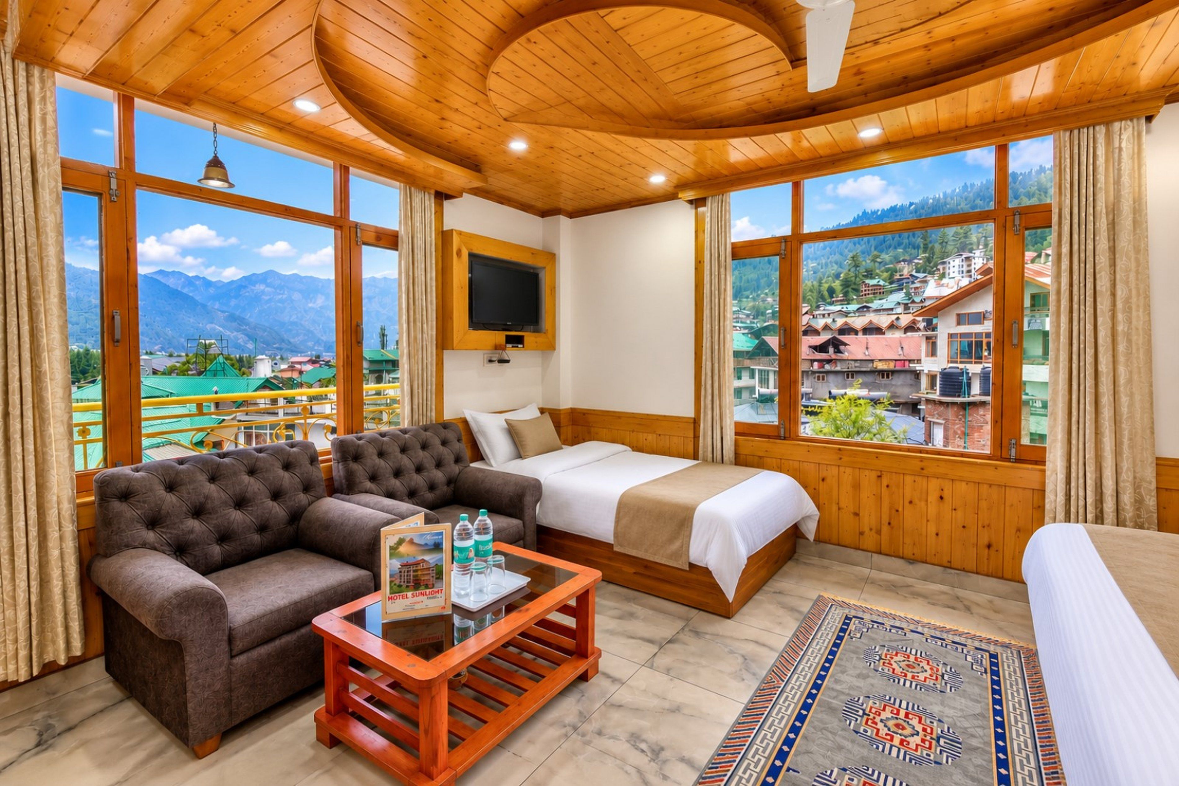 A hotel room with a bed, a sofa, a TV, and a view of mountains and a village.
