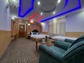 Habitación de hotel con cama, sofá, piso de madera, ventilador de techo y ventana con cortinas.