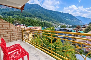Un balcon avec une chaise rouge, une rambarde jaune et une vue sur un paysage montagneux parsemé de bâtiments.