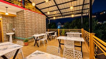 An outdoor patio with tables and chairs, a brick wall, and a view of the surrounding area at night.