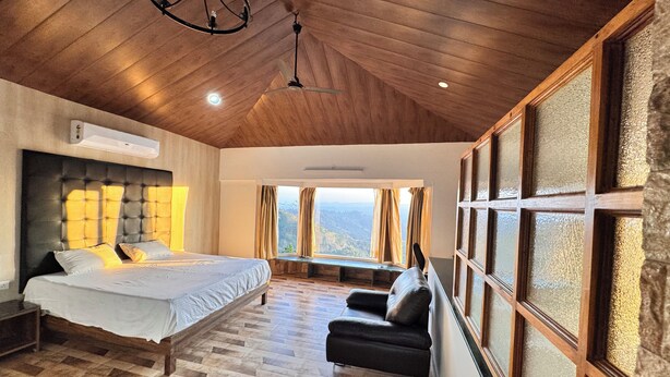 A bedroom with a bed, a bench, a chair, and large windows with curtains.