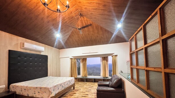 Un dormitorio con una cama, un sillón de cuero, una ventana con cortinas y un techo de madera.