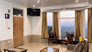A spacious living room with a ceiling fan, a flat-screen TV, and a large window with curtains.